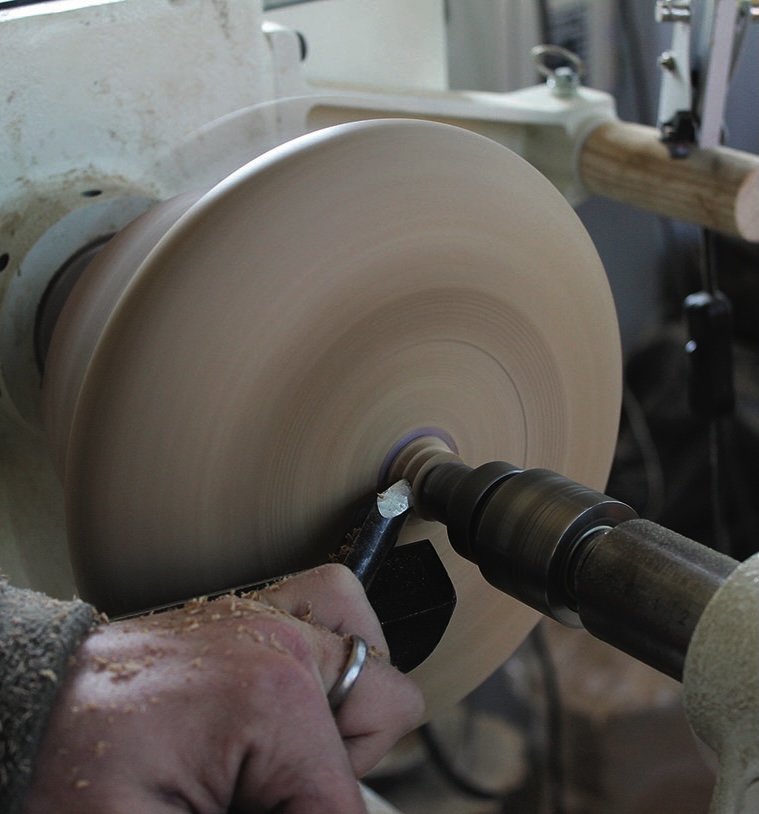 Woodturning on a lathe with cutting tool.