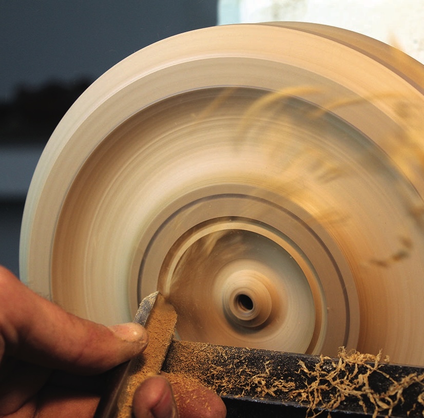 Woodturning tool shaping spinning wooden bowl.