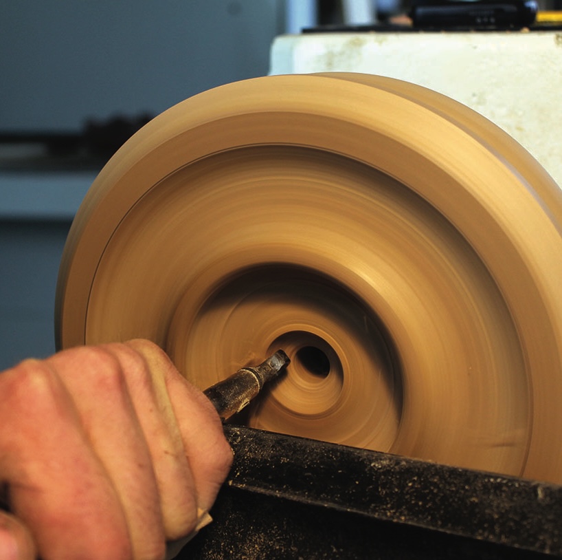 Person woodturning a wooden bowl on lathe machine.