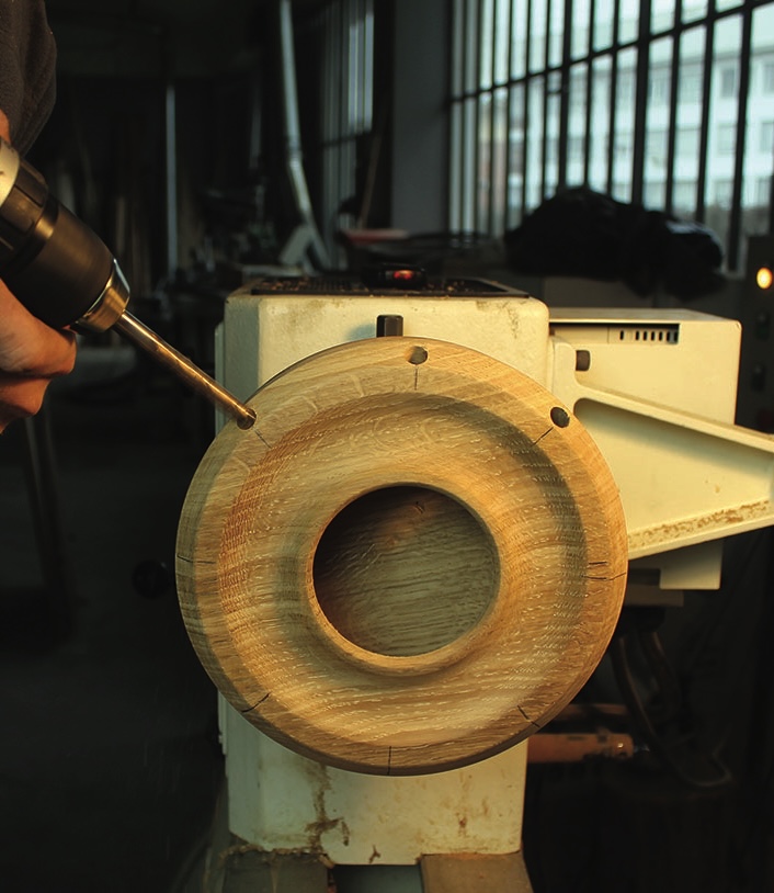 Person drilling into wooden object on lathe machine.