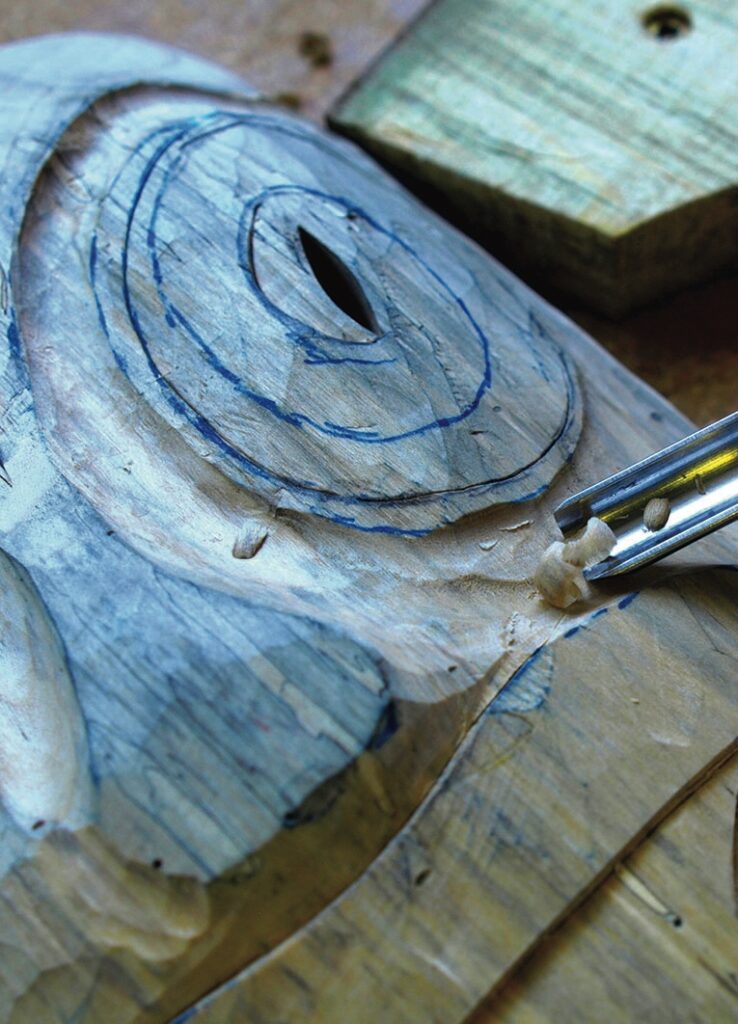 Chisel carving an eye shape into a wooden sculpture