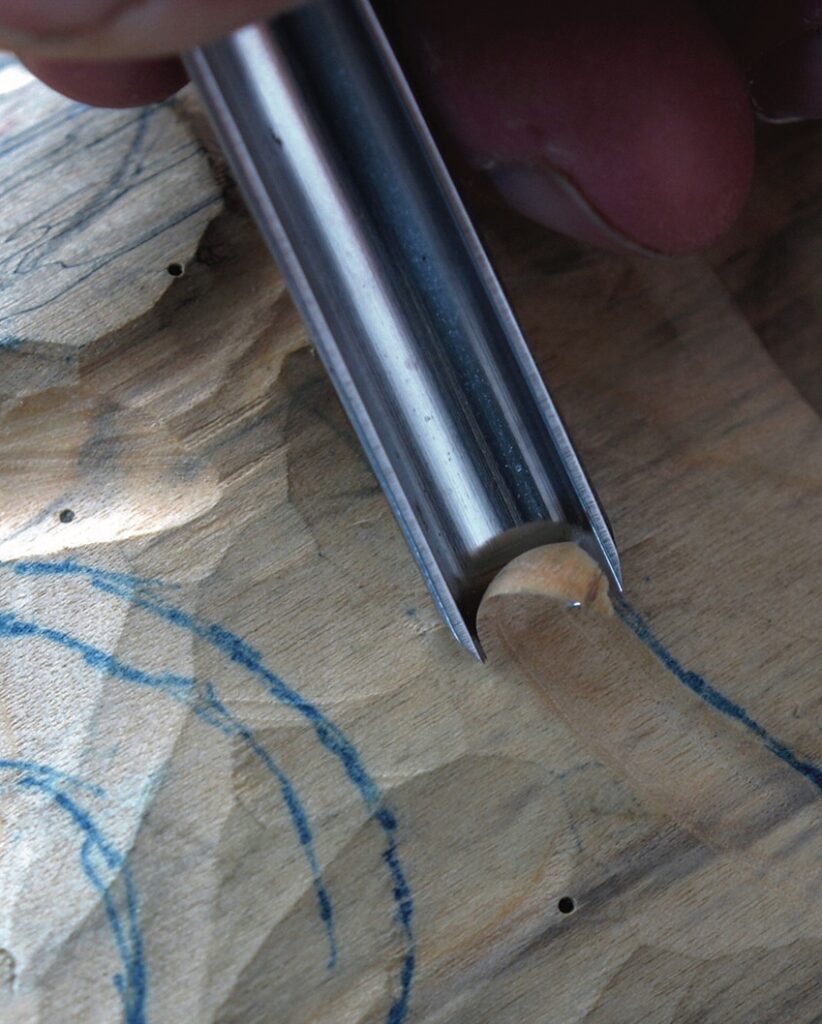 Hand using a gouge to carve marked wood