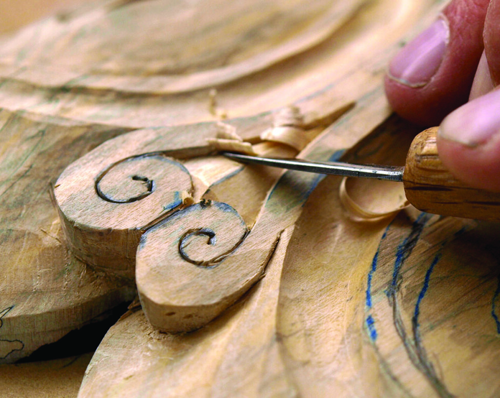 Craftsperson carving wooden decorative scrollwork with a chisel