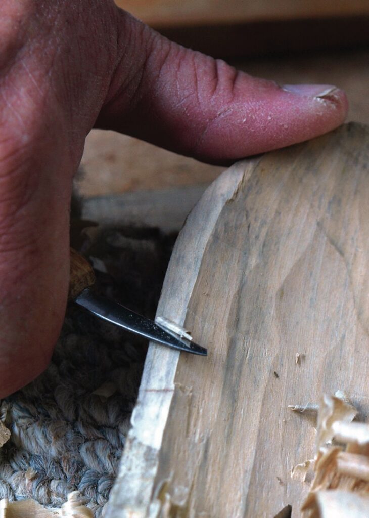 Hand carving a wooden bowl rim with chisel