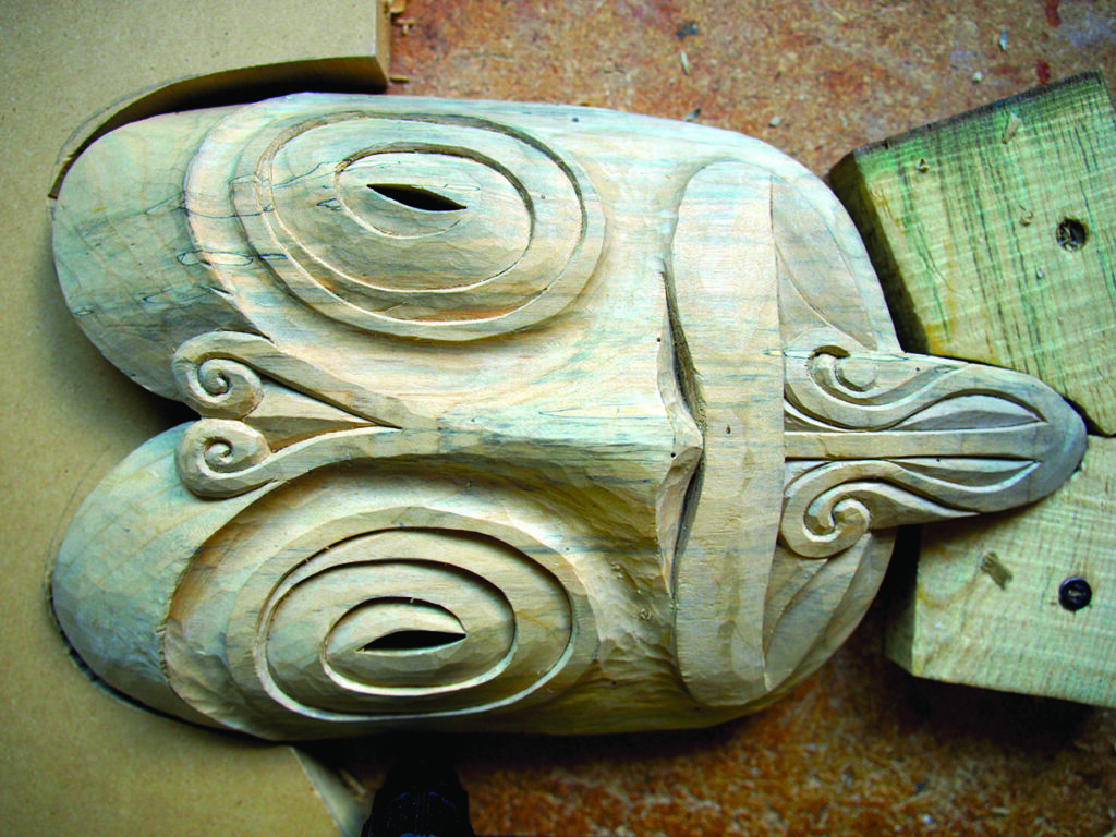 Unfinished carved wooden mask with spiral eyes and stylised nose