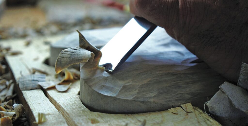 Craftsperson carving a wooden bowl with hand tools