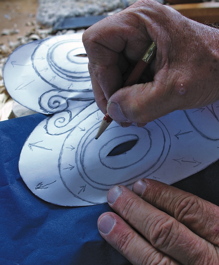 Hands sketching a decorative mask pattern with pencil