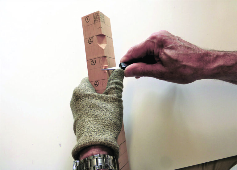 Person carving wood with glove and knife.