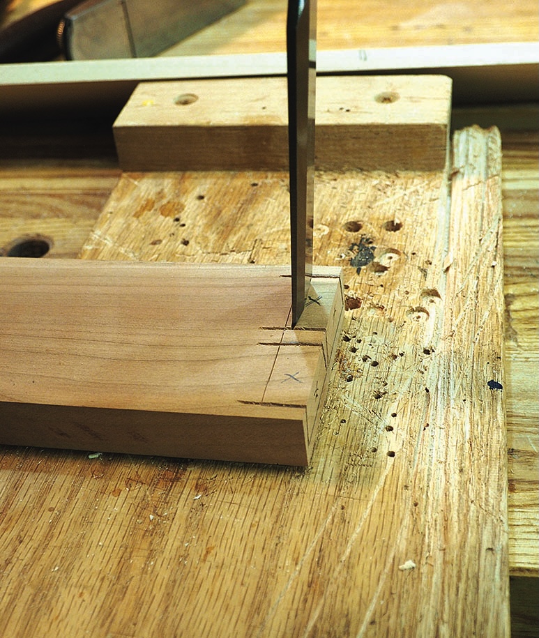 Handsaw cutting marked timber joint on workbench