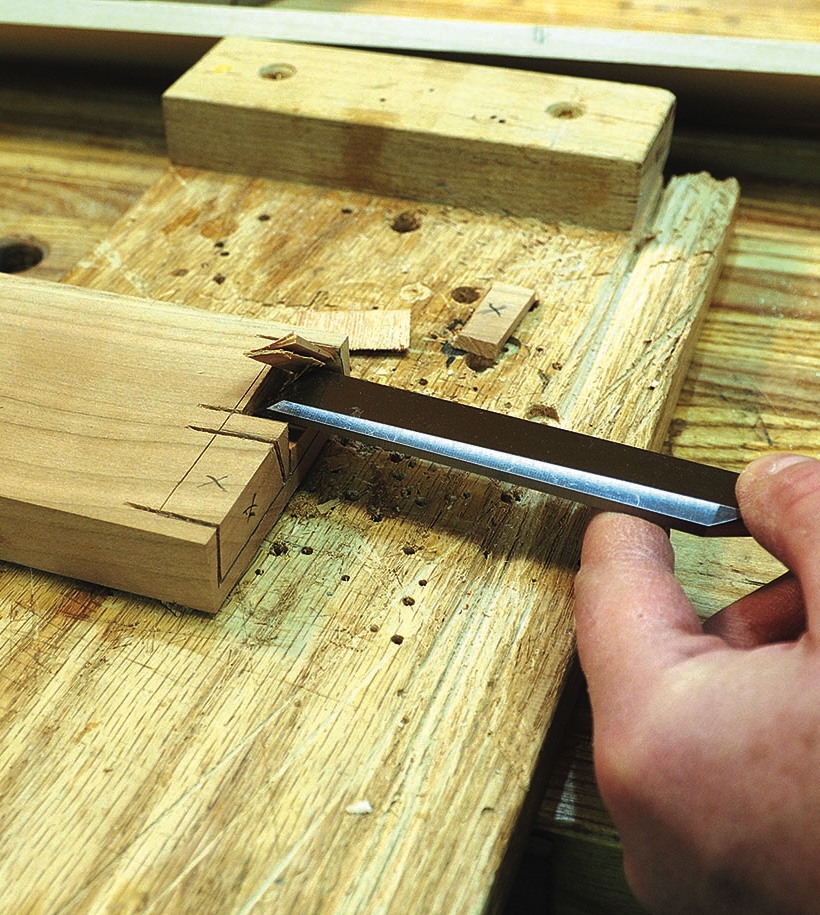 Hand chiselling a marked wood joint on workbench