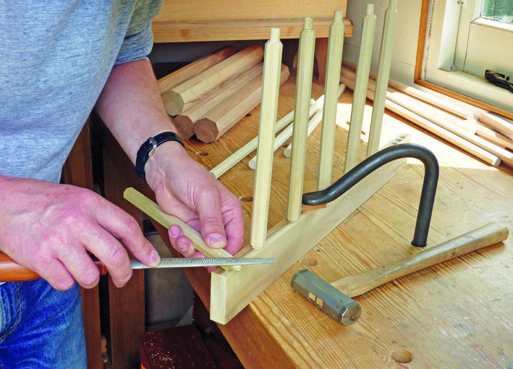 Craftsman filing wooden chair spindle in workshop.
