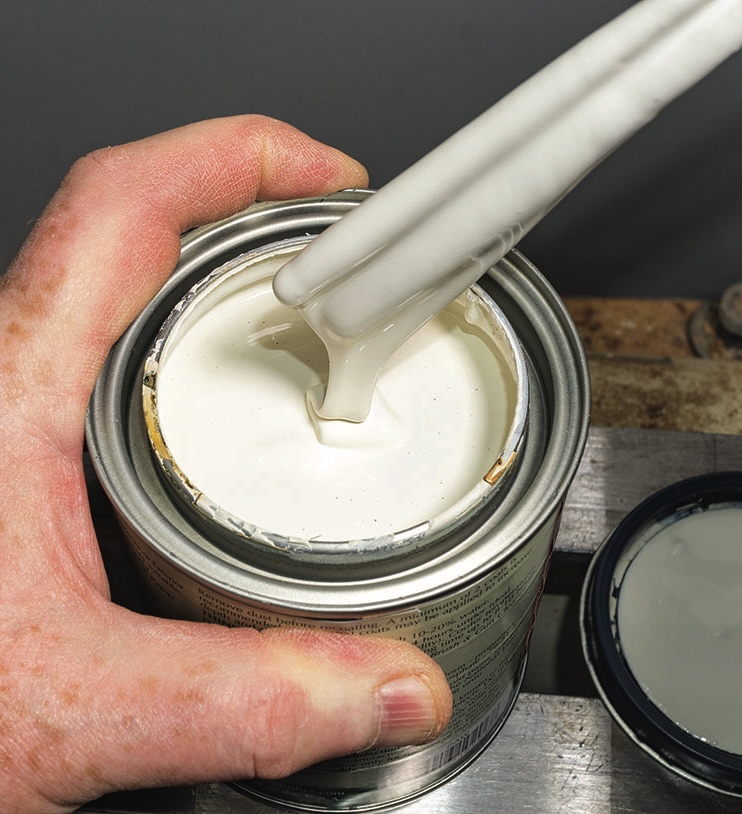 Stirring white paint in a metal tin.