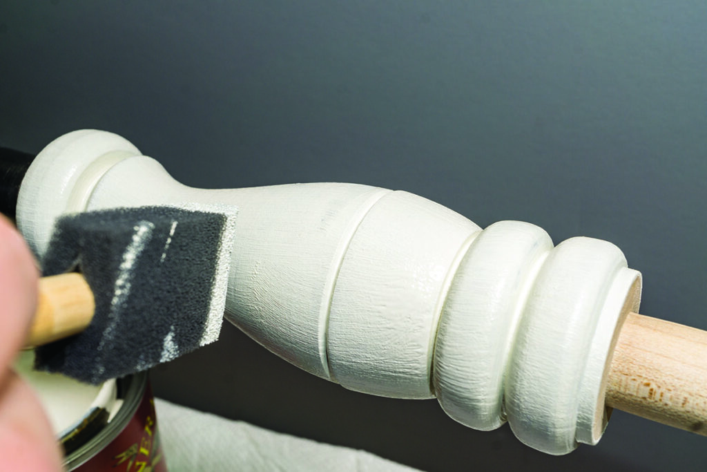 Applying white paint on wooden furniture with brush
