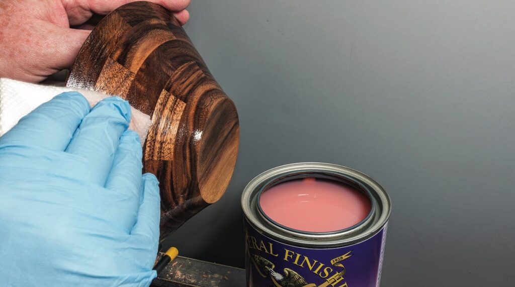 Applying finish to wooden bowl beside paint can.