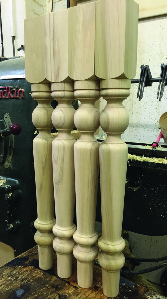 Four turned wooden table legs beside a lathe