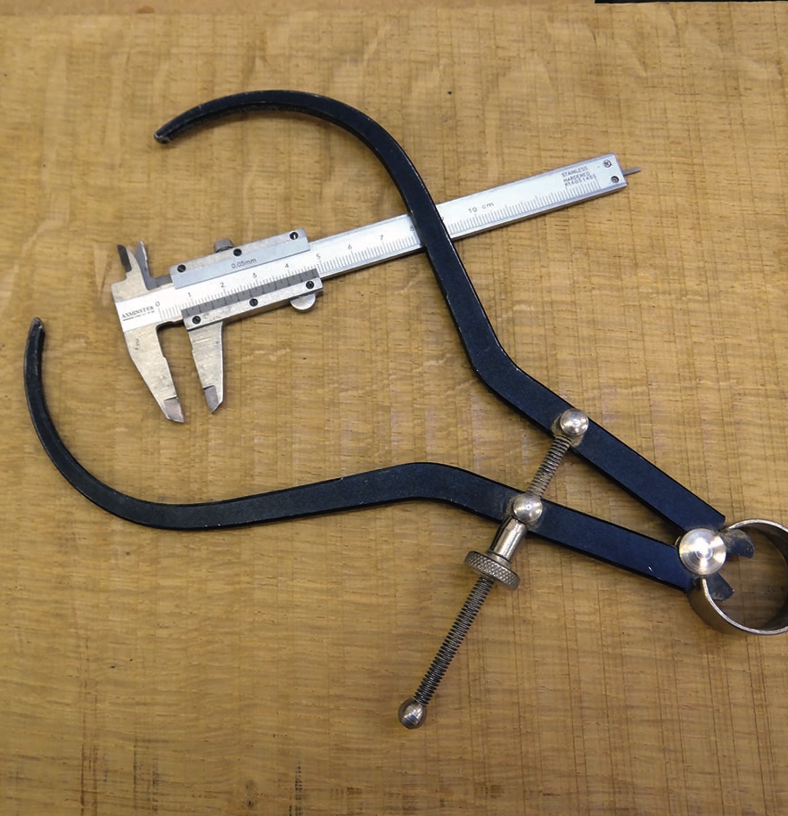 Black curved callipers beside a vernier caliper on wood