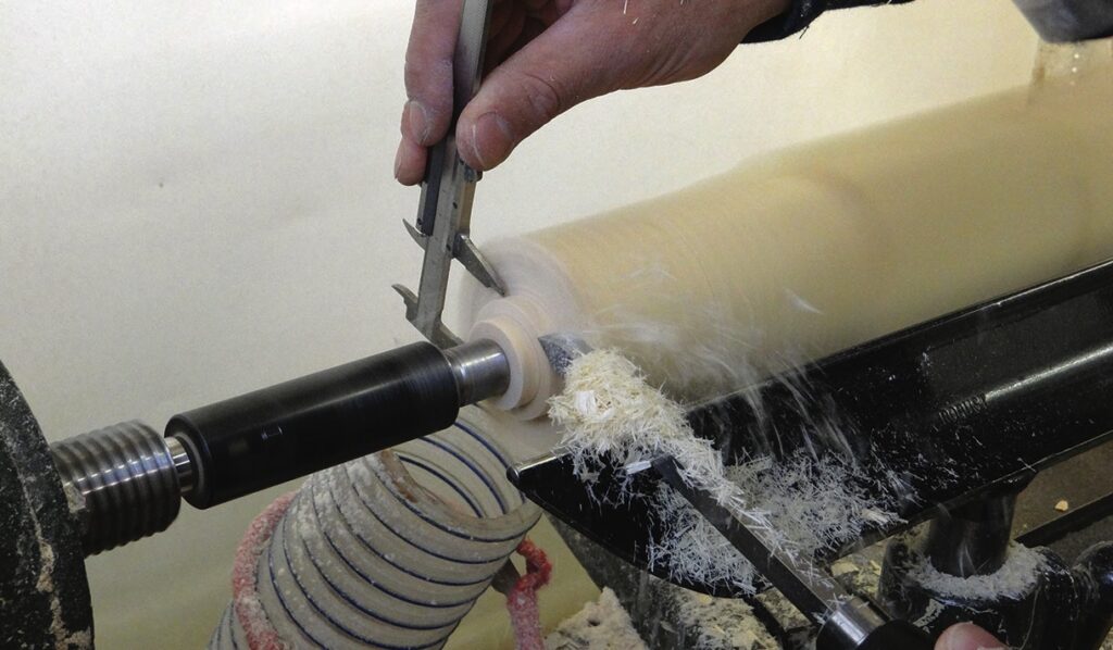 Woodworker measuring a spinning bowl blank on a lathe