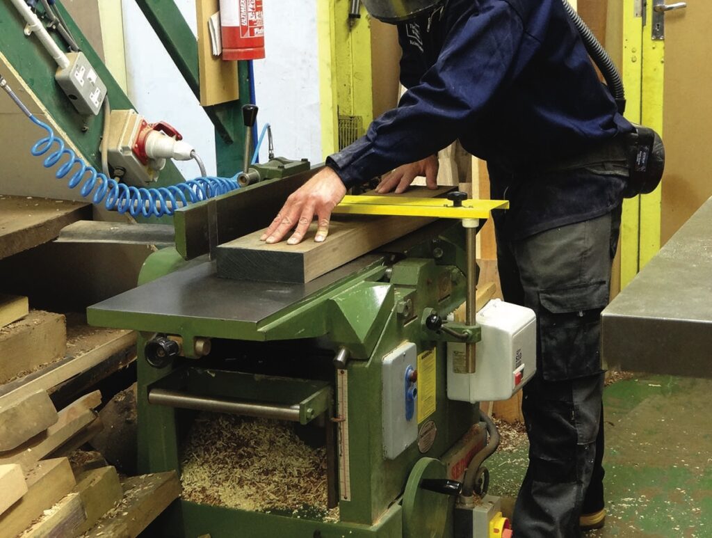 Woodworker planing timber on a green woodworking machine