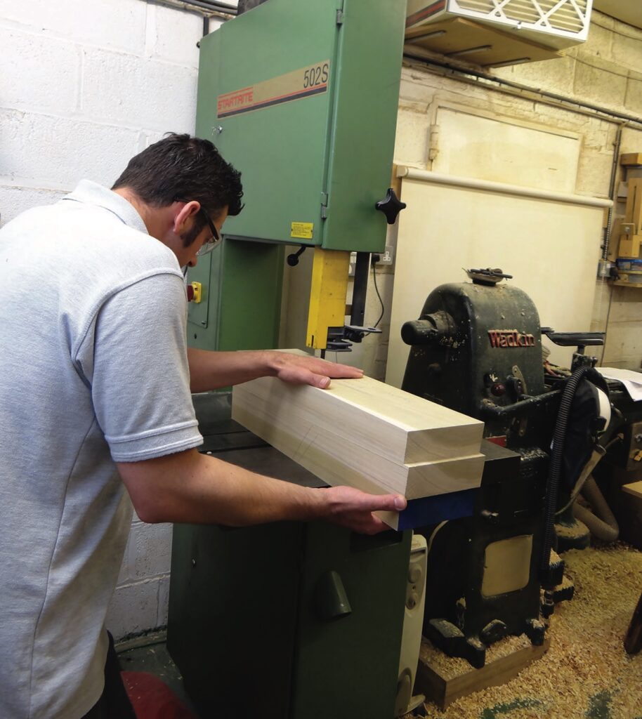 Woodworker positioning timber at a bandsaw in workshop