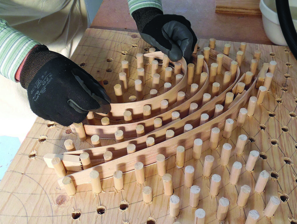 Gloved hands bending wooden strips around pegs