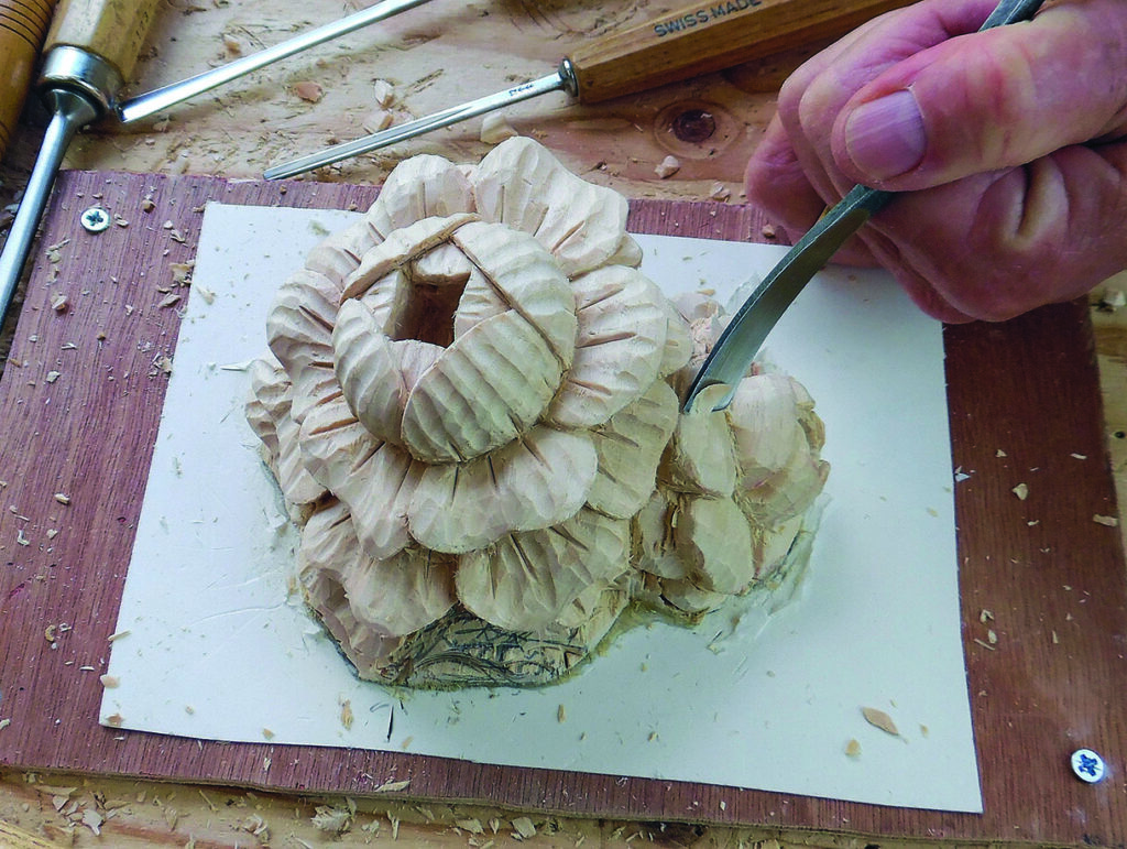 Craftsperson carving wooden flower sculpture with chisel