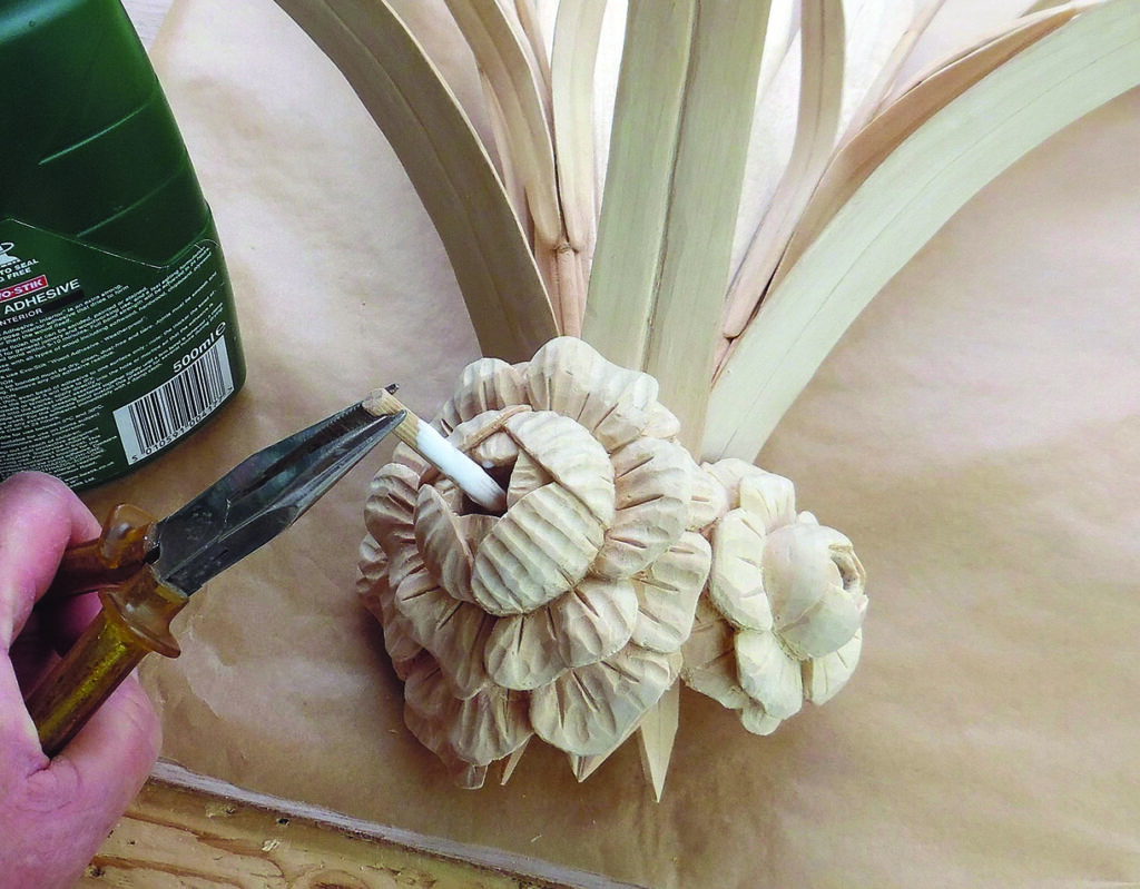 Applying adhesive to carved wooden flower arrangement