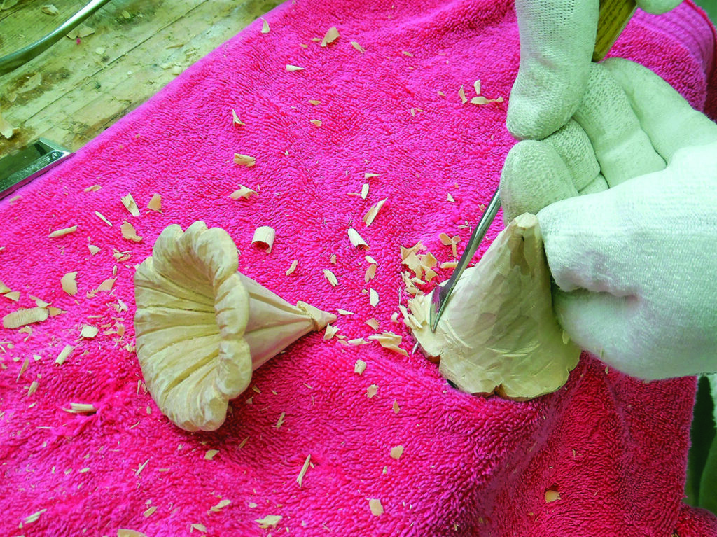 Gloved hands carving a wooden flower on pink towel