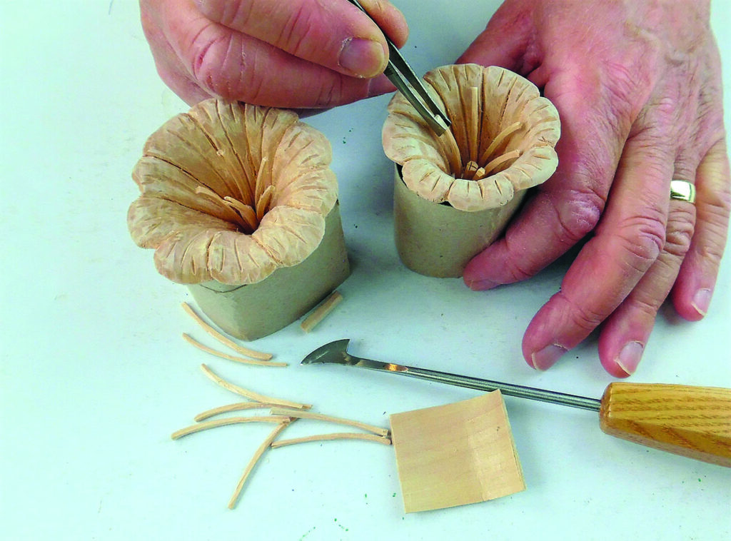 Hands shaping wooden flowers from carved wood shavings