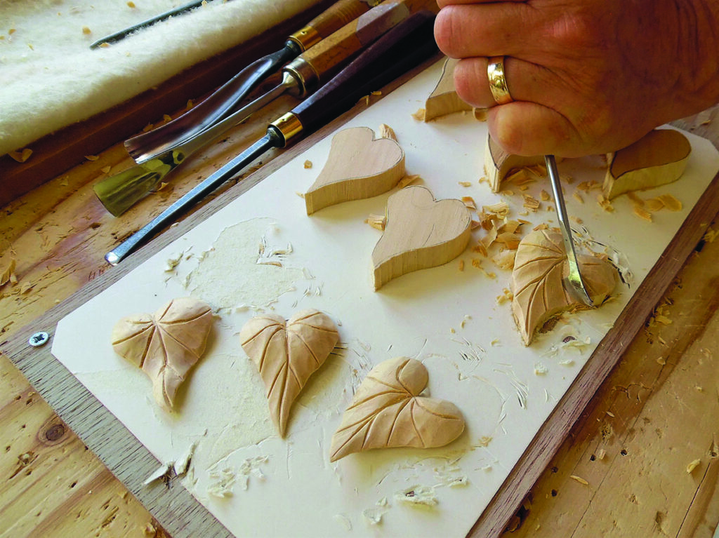 Woodworker carving leaf-shaped wooden ornaments with a gouge
