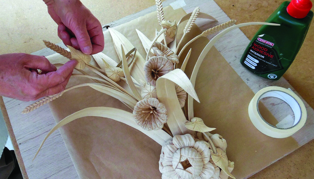 Hands arranging handmade wooden flowers and wheat stems
