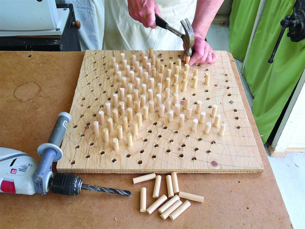 Craftsperson hammering wooden dowels into drilled board