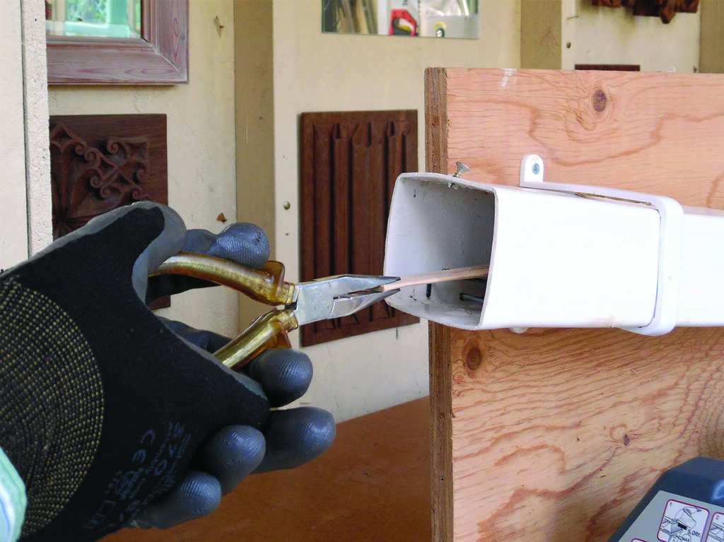 Gloved hand using pliers to repair a gutter fitting