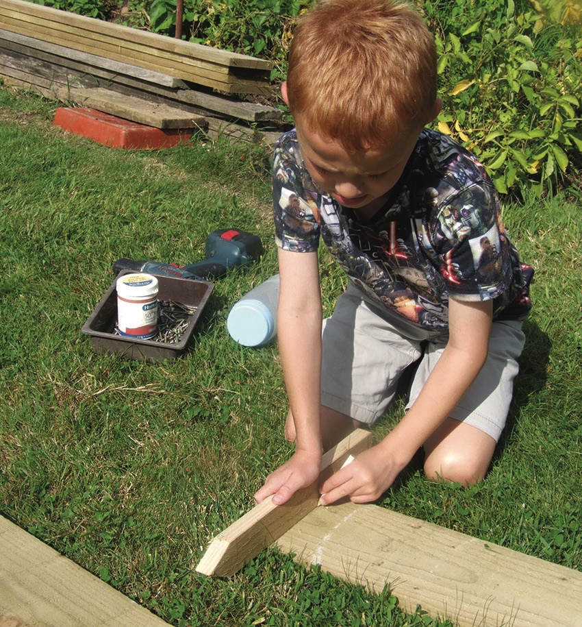 Boy assembling wooden garden structure on grass