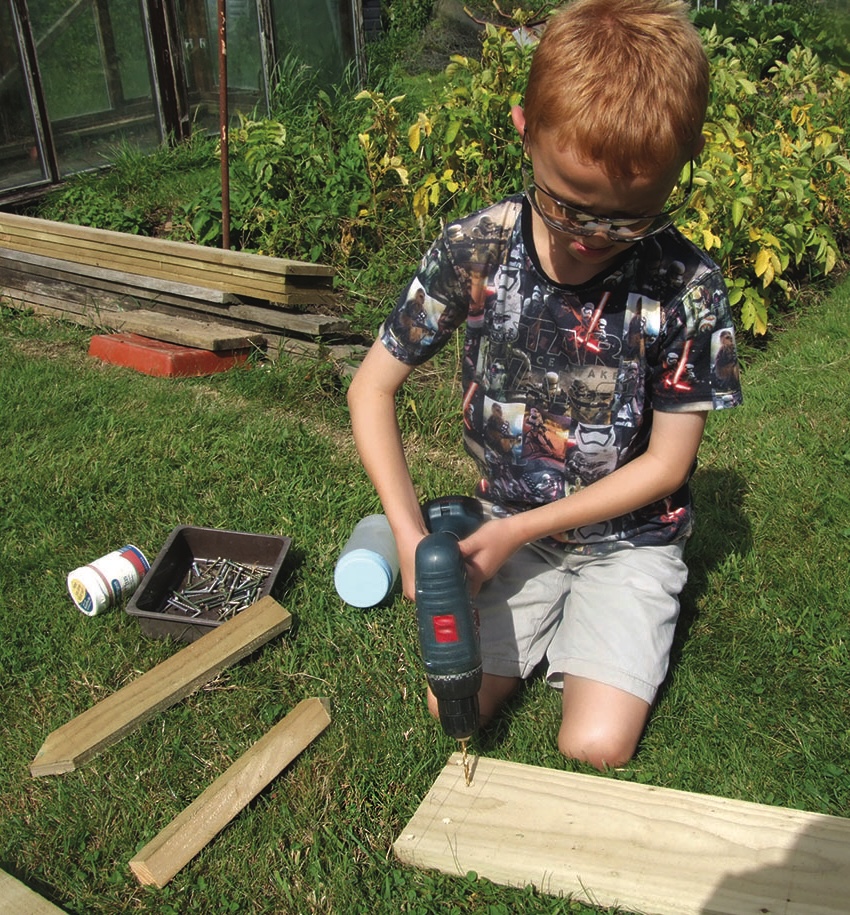 Boy wearing goggles drills timber in a garden