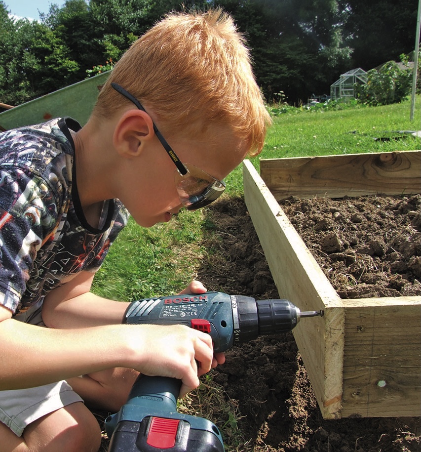 Boy drilling wooden raised garden bed outdoors