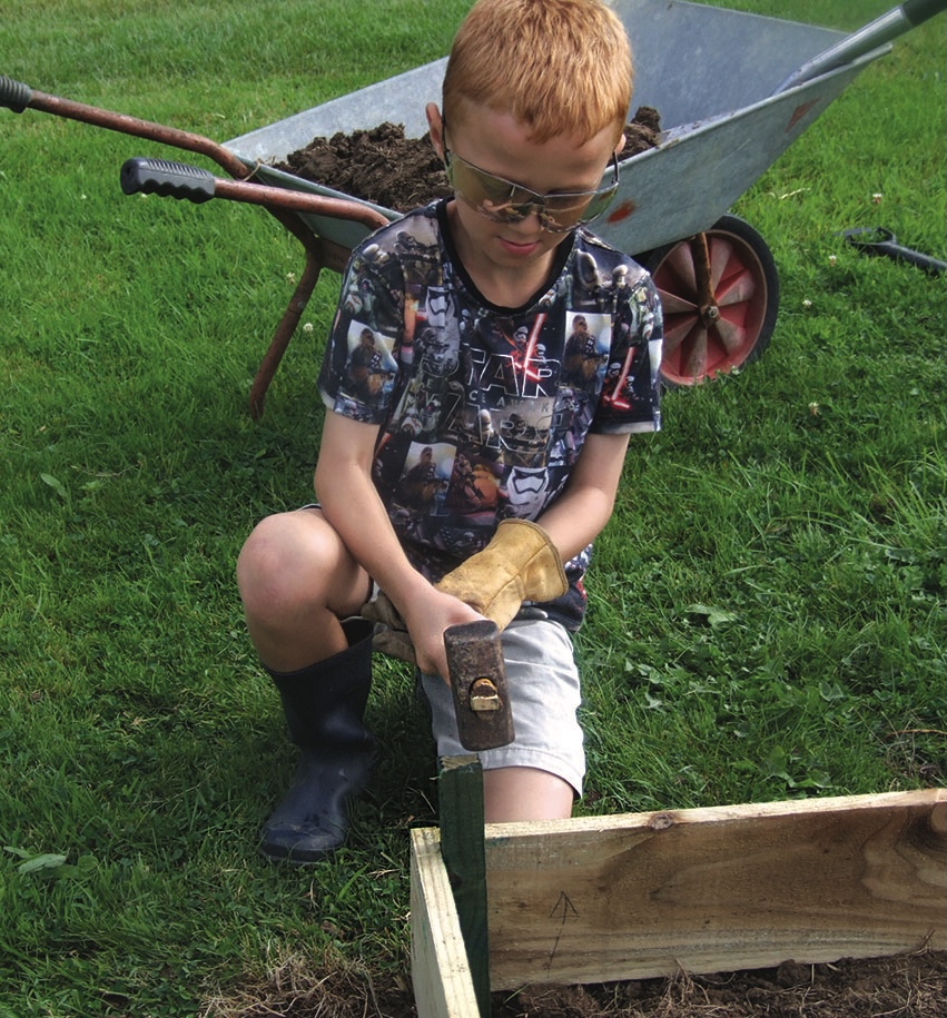 Boy hammering wooden raised bed beside wheelbarrow
