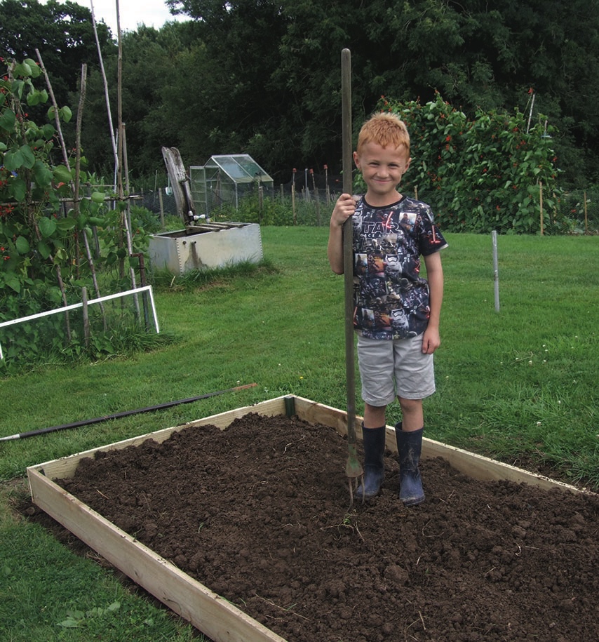 Young boy holding spade beside freshly filled raised garden bed